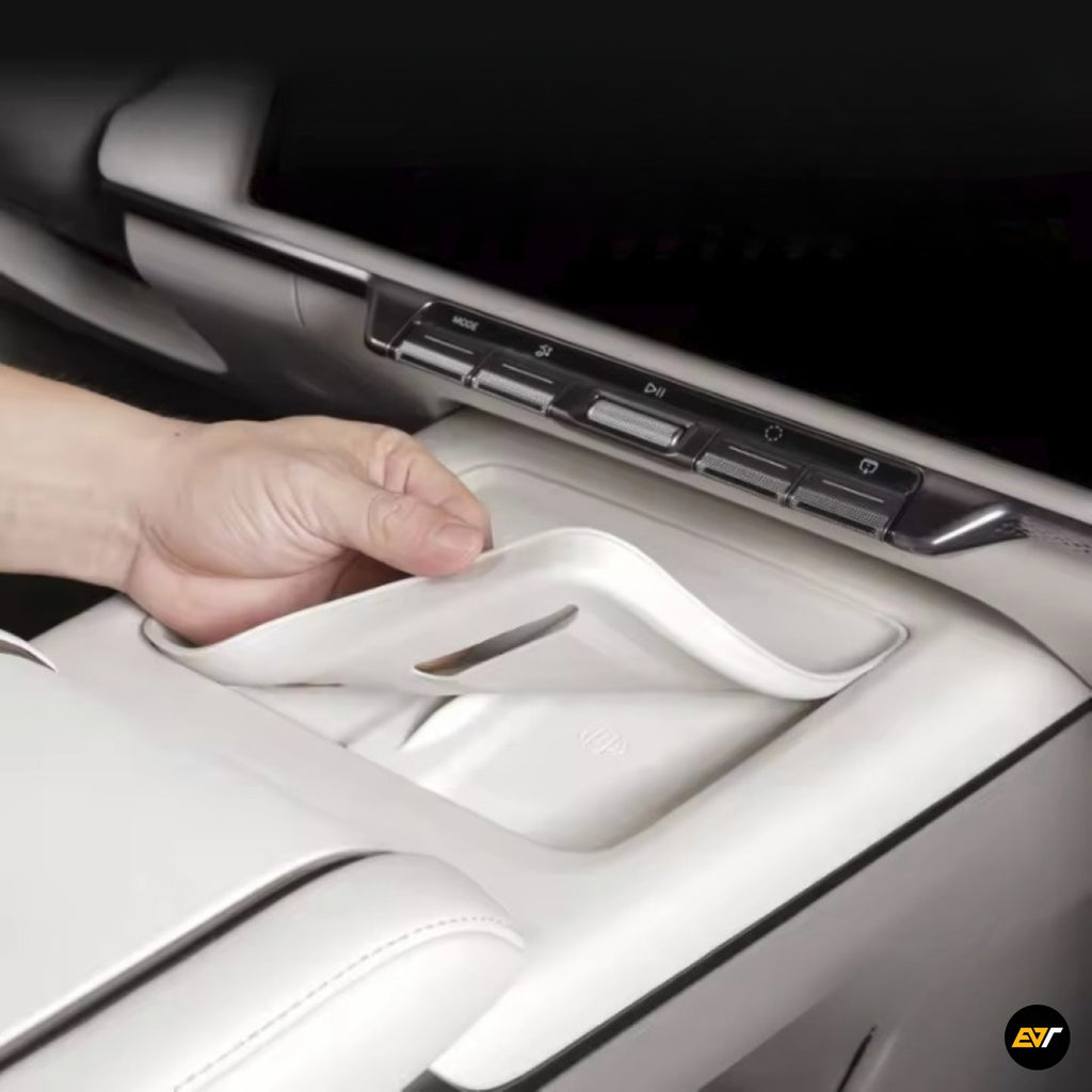 Hand lifting white silicone anti-slip pad inside a vehicle's centre console compartment with control buttons above.